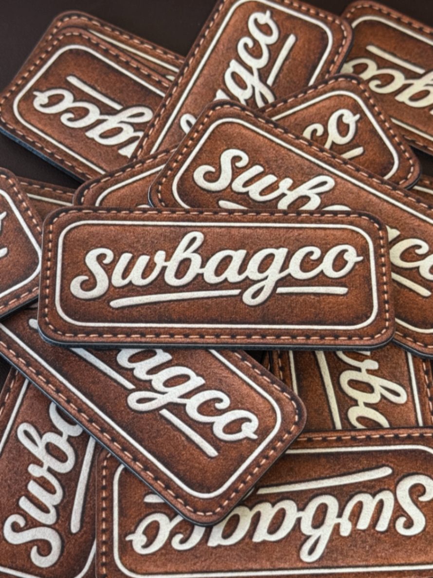 Pile of stitched leather patches embossed with the swbagco script logo